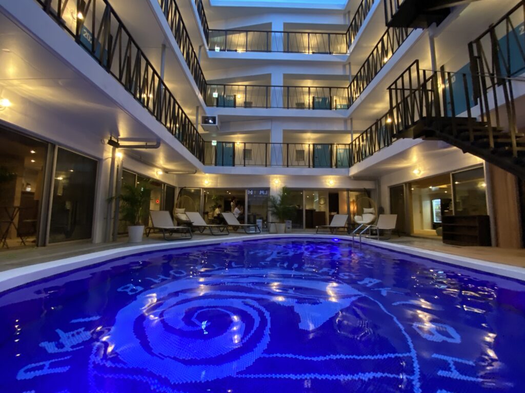 夜のホテル中庭にあるライトアップされたプール。モザイク模様の床デザインと周囲の客室バルコニー、ラウンジチェアが並ぶ落ち着いた空間。