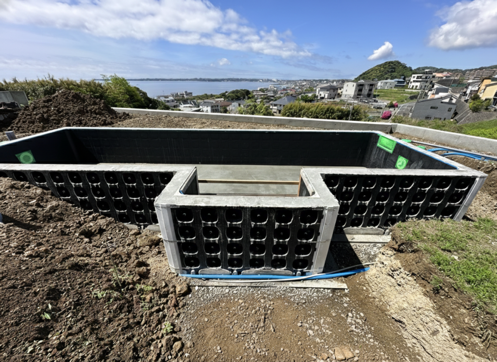 「湘南の塩害エリアで進むマジラインプールの躯体工事。250mm厚の自立型躯体パネルにダブル配筋を施した強固なモノコック構造が組み上がり、地中に埋め込まず自立する高強度構造が、海を望む住宅地の斜面で施工されている様子を写した写真