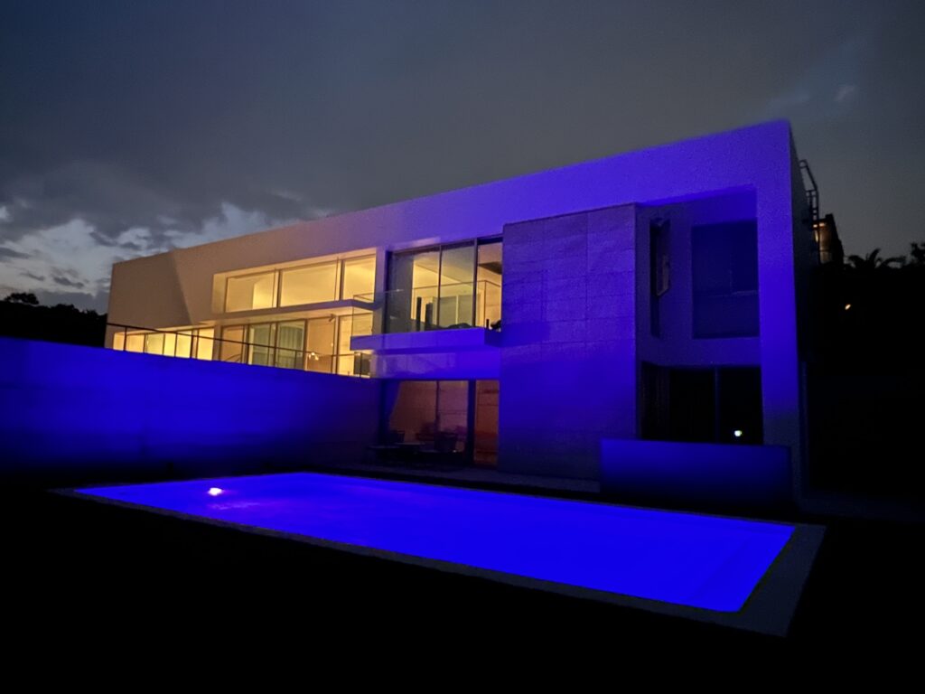逗子市の別荘に設置したナイトプール。青いライトで照らされたプールとガラス張りのモダン住宅が映える夜の外観
